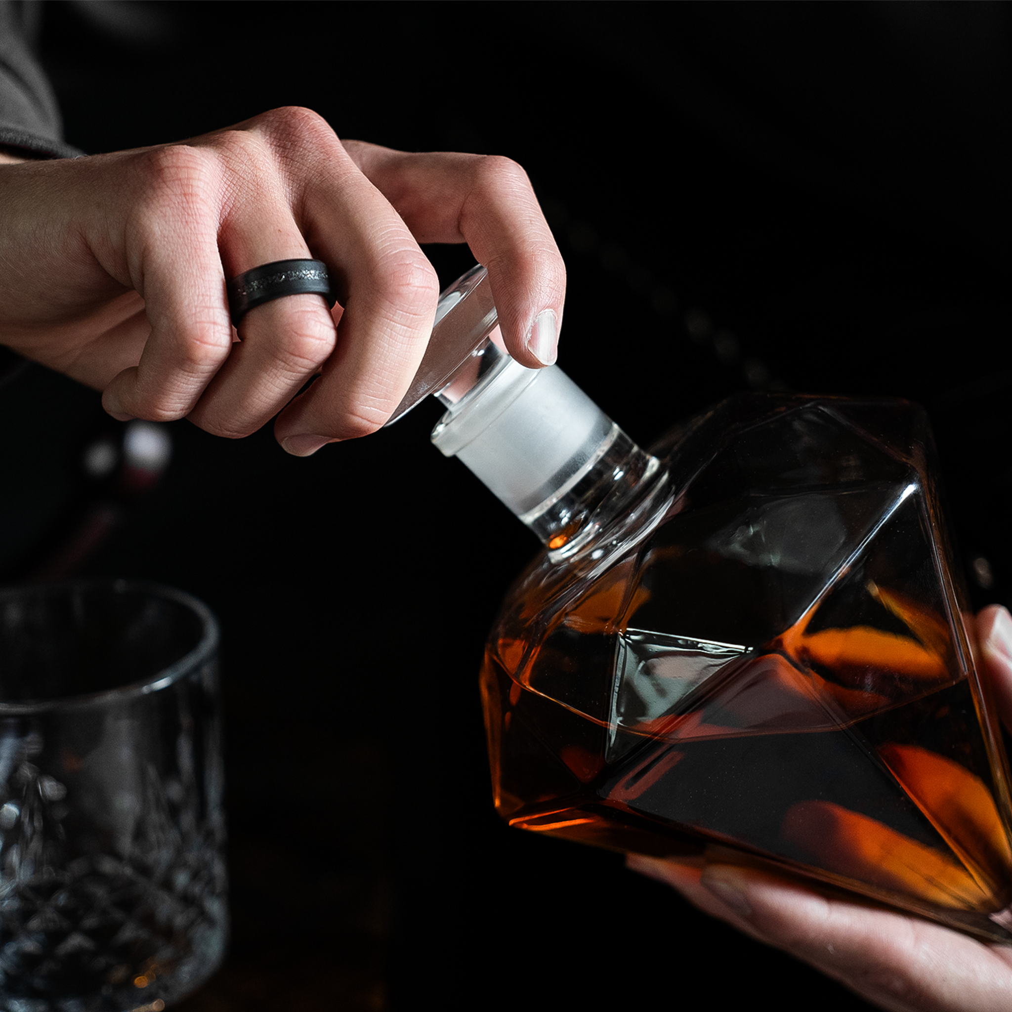 Meteorite Inlay Black Diamond Wedding Ring on hand, holding a whiskey decanter