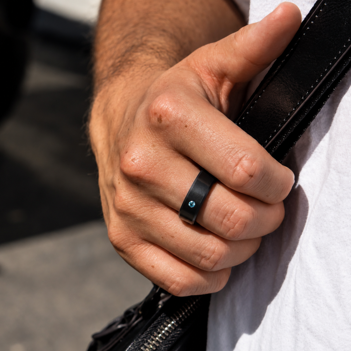 8mm ARES Stone Accent solid black diamond ring with a Blue diamond, worn on a hand holding a black leather strap.