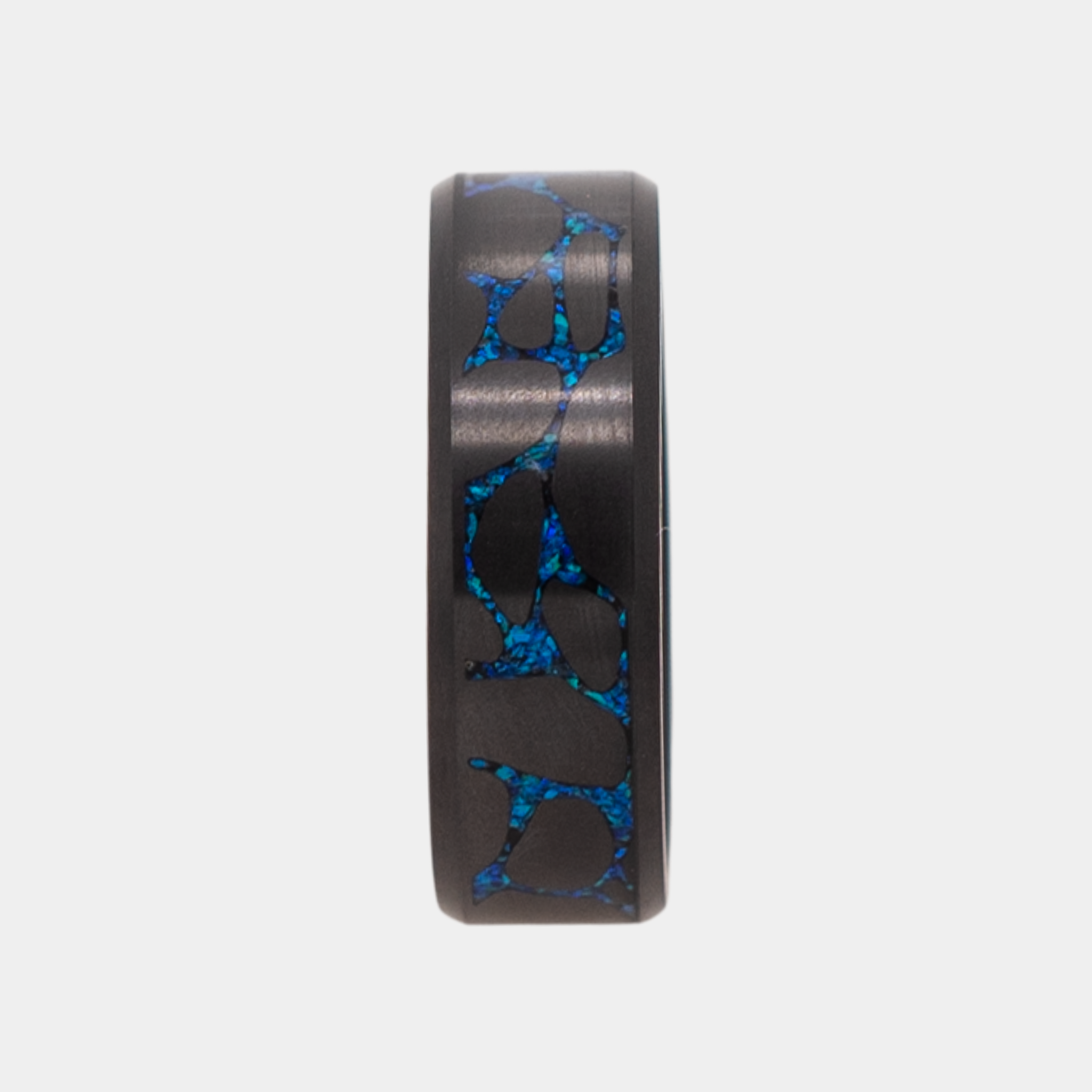 Vertical shot of Solid Black Diamond ring with laser engraved river stone inlay filled with blue opal on a light gray background