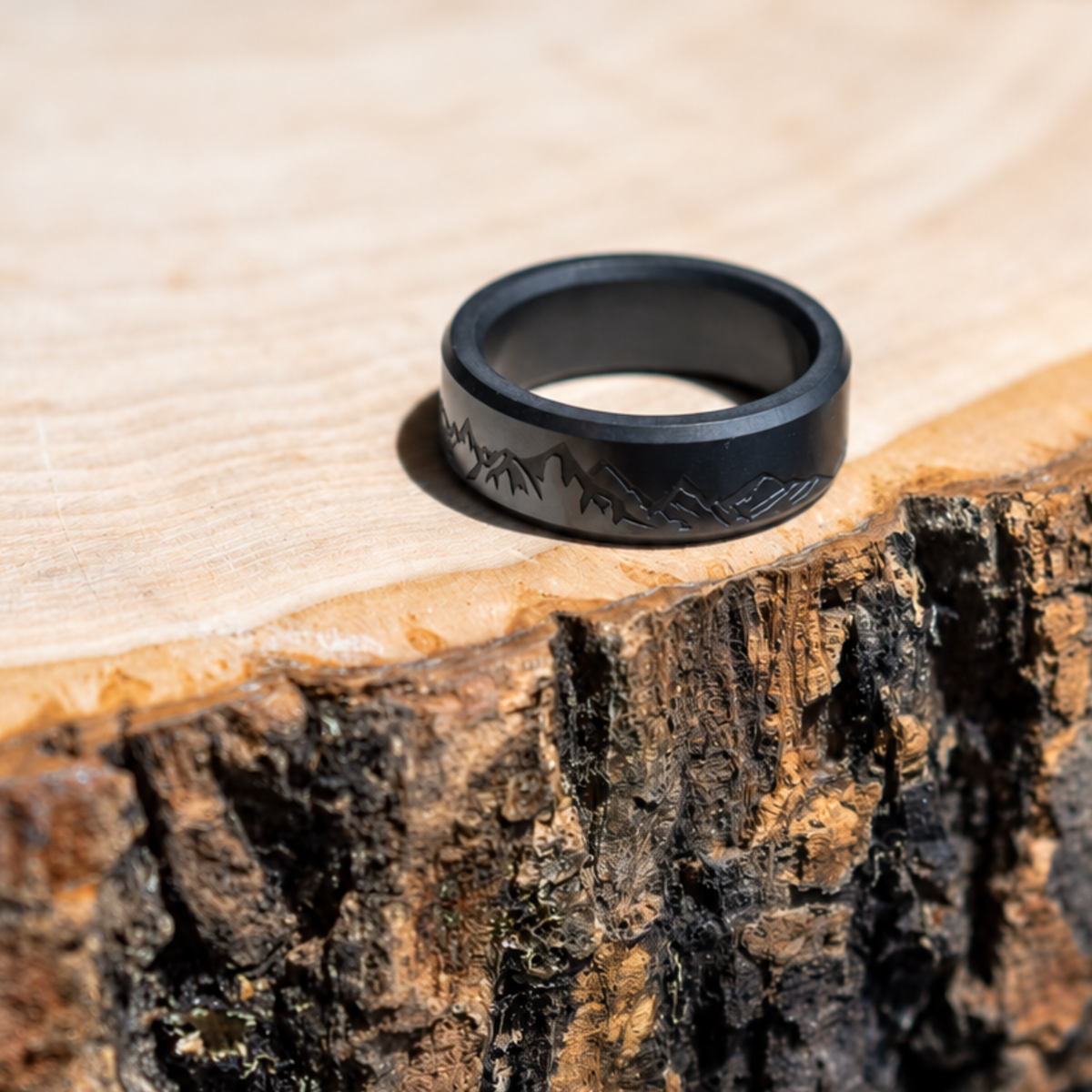 ARES solid black diamond ring with an example laser-engraved mountain range, resting on a wood slice.